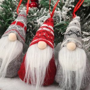 Detailed close-up of three knitted Christmas gnomes hanging on a snowy tree branch