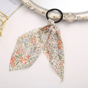Close-up of floral bow ribbon hair tie with orange and blue flowers on cream fabric
