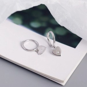 Detail of S925 silver heart hoop earrings with star-set zircon on white paper