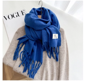 Detail of blue knitted scarf with fringes and brand label on a wooden hanger