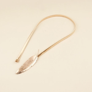 Macro detail of golden metal spring waist chain with intricate feather-shaped ornament