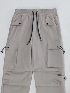 Detail of light khaki parachute pants with elastic drawstring waist and large cargo pockets
