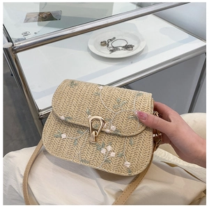 Close-up of beige straw saddle bag featuring floral embroidery and gold metal clasp lock