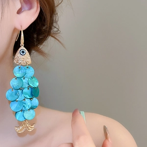 Macro shot of fish-shaped earrings with blue sequins and golden metal on model