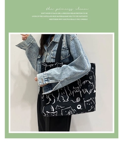 Close-up of a large black canvas tote bag featuring white hand-drawn cat illustrations