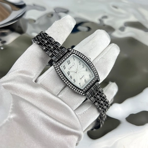 Close-up of a tonneau emerald quartz watch with diamond bezel held by a gloved hand