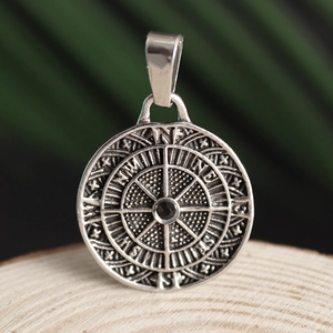 Macro view of silver compass pendant with black gemstone on a wooden display stand