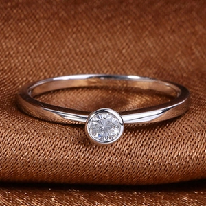Minimalist silver-toned bezel-set round sparkling gemstone ring on brown texture