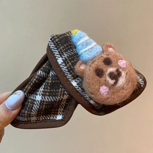 Detailed close-up of a brown plaid hair clip featuring a small blue-hatted felt bear charm