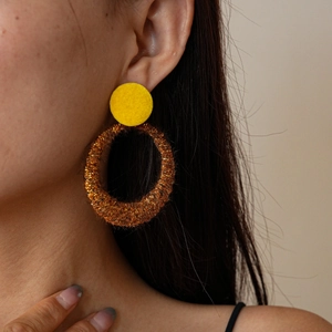 Close-up of a gold textured circular earring with yellow studs worn on a female model