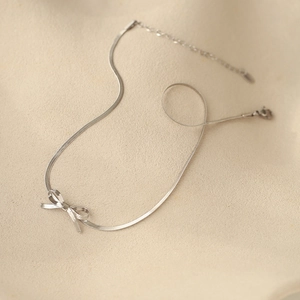Detailed view of silver bow snake chain necklace with lobster clasp on beige surface