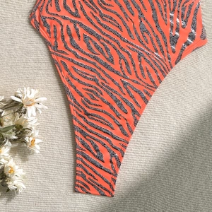 Detail of orange zebra print swimsuit showing high-cut leg and elastic fabric texture