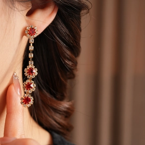 Close-up of gold tassel earrings with red gemstones and clear crystals on a model