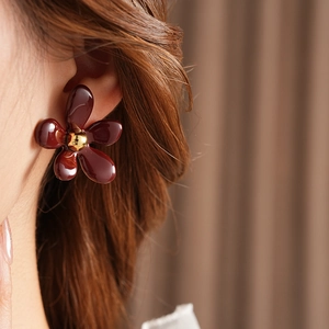 Close-up of a vintage dark red resin flower earring with a gold center on a model's ear