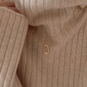 Minimalist gold irregular geometric oval pendant necklace on a beige knit sweater background