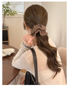 Detailed close-up of brown knitted scrunchie texture worn on a ponytail in warm lighting