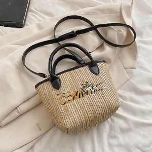 Close-up of woven straw bucket bag with black leather handle and tiger embroidery