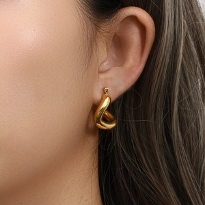 Close-up of golden curved double-layer C-shaped hoop earrings with metal strap texture
