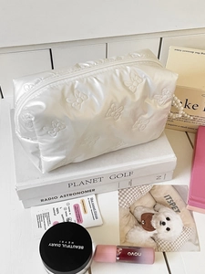 Detail of white satin cosmetic bag featuring embossed bow texture and pearl luster finish