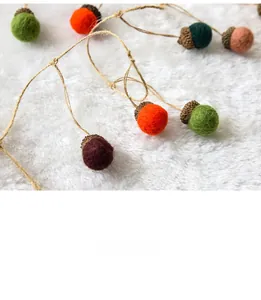 Detail of wool felt acorn pendants with natural rope hanging on white plush background