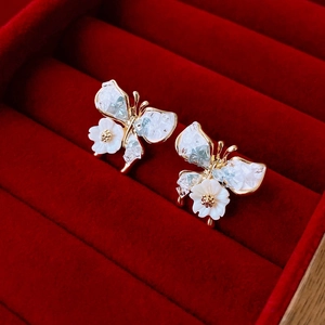 Detailed macro view of golden butterfly earrings with crystal inlay and white floral accents