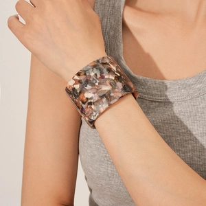 Detailed close-up of a wide floral acetate cuff bangle with marbled texture on a wrist