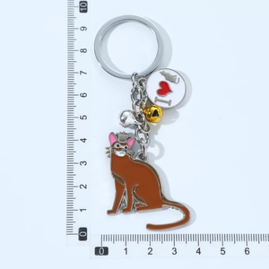 Detail of brown cat keychain with bells, logo tag, and measuring scale reference