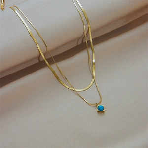 Double-layered gold titanium necklace with square turquoise pendant on beige fabric