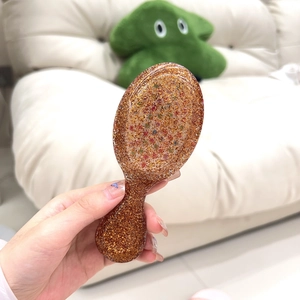 Detail view of mini portable hair brush with gold glitter held in hand for size context