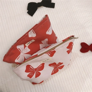 Detail view of canvas makeup bags with red and white bow patterns and metal zippers
