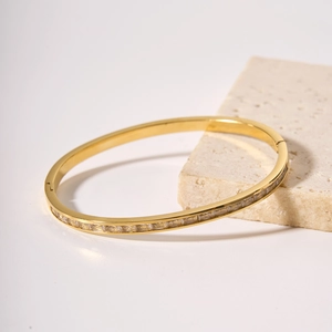 Gold plated stainless steel bangle with square zircon inlay on a beige stone stand