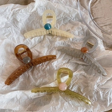 Close-up of four large resin shark hair clips in milk coffee, amber, gray, and green colors