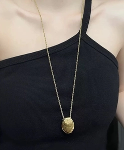 Detail shot of a long gold teardrop pendant necklace on model highlighting minimalist style