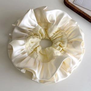 Close-up of ruffled cream satin scrunchie with layered fabric texture on white surface