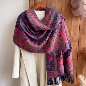 Detail of burgundy paisley scarf with tassels draped over a stylish white coat