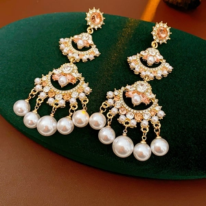 Macro detail of fan-shaped fringe earrings with pearls and rhinestones on green velvet