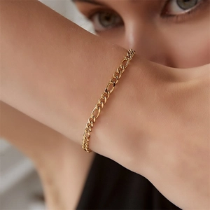 Close-up of a gold-plated stainless steel Figaro chain bracelet worn on a female wrist