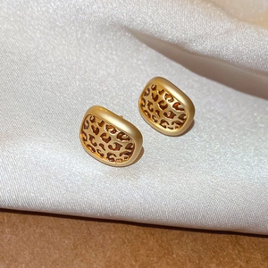 Detail shot of vintage golden leopard print oval earrings on white silk fabric