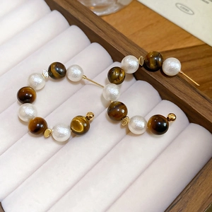 Gros plan de boucles d'oreilles C rétro avec perles œil de tigre et perles nacrées