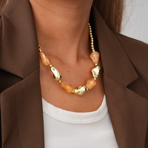 Detail of irregular golden metal elements and orange marble resin beads on a long necklace