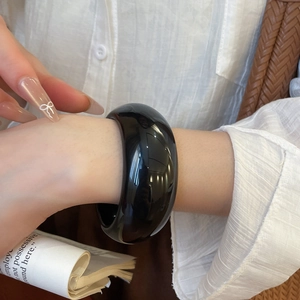 Polished black resin bangle bracelet with wide circular geometry on woman's wrist