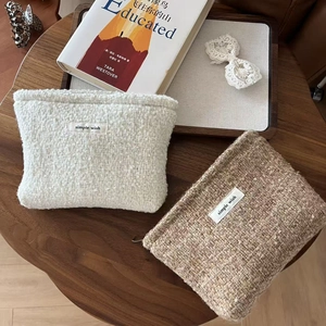 Elegant tweed cosmetic bags in beige and light brown shown on a rustic wooden table