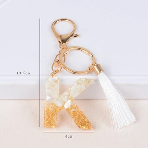 Detail of letter K keychain featuring white resin stones, gold foil, and long silk tassel
