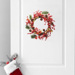 Christmas wreath with red berries and pine cones hanging on a white door with a holiday stocking