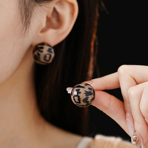 Macro detail of round leopard print stud earrings worn on ear and held by hand