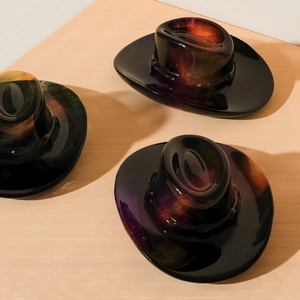 Cowboy hat shaped glass ornaments with nebula galaxy swirls on a wooden surface