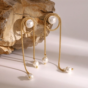 Golden stainless steel long fringe earrings with white pearls on a natural stone surface
