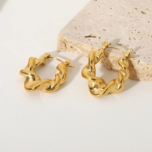 Detail of gold plated twisted hoop earrings on a textured stone decorative background