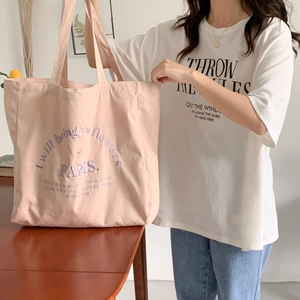 Pink canvas tote bag featuring embroidered letters carried by a model in a cozy room