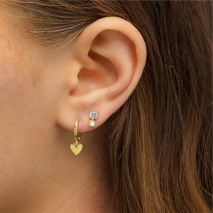Macro view of gold heart charm hoop earring and double diamond stud worn by a model